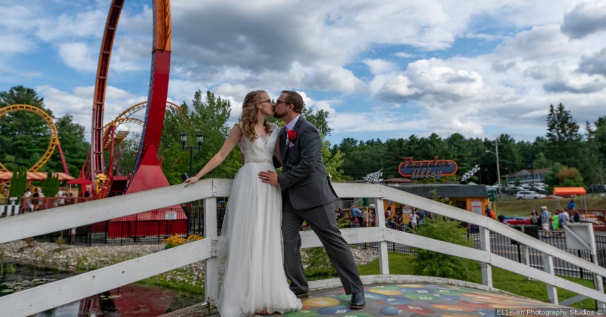 couple kissing in wedding attire in front of roller coaster