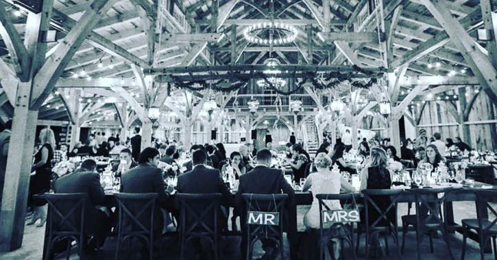 black and white artsy photo of bride and groom and guests seated in a barn