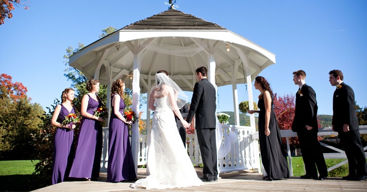 bride and groom holding hands in front of a gazebo with their wedding party