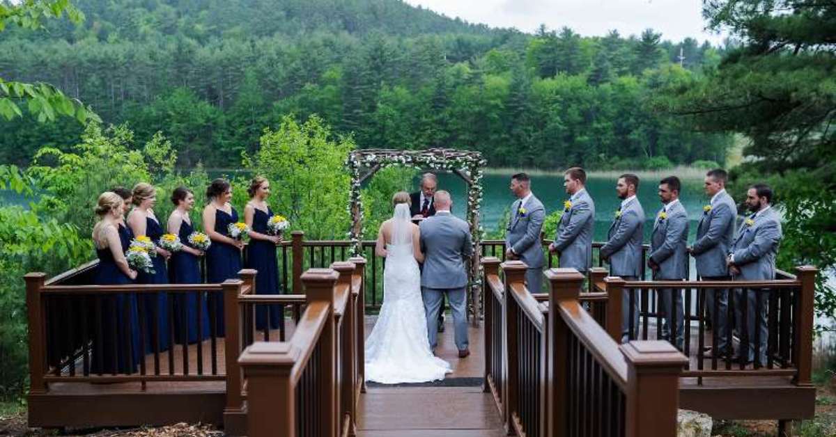 a couple getting married on a deck in front of a beautiful view with their wedding party looking on 