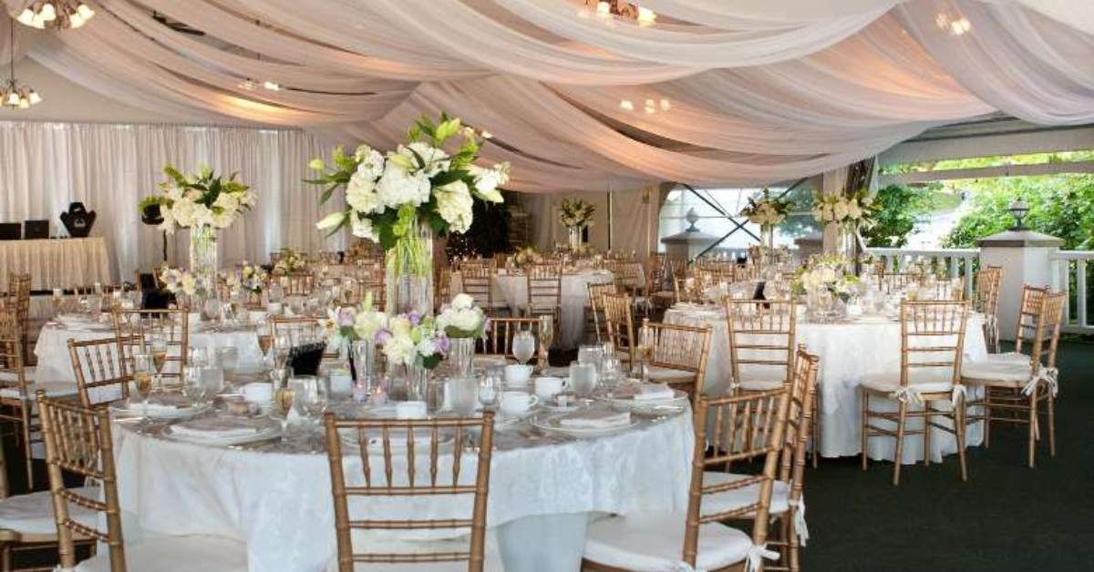wedding reception setup with chairs and tables in a white tent