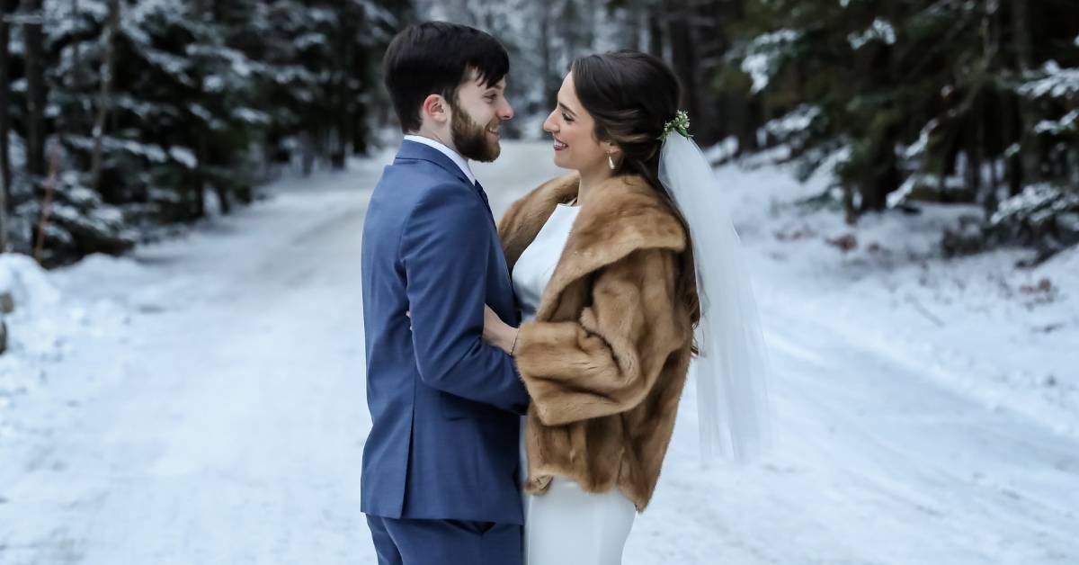 bride and groom look at each other while standing in the snow